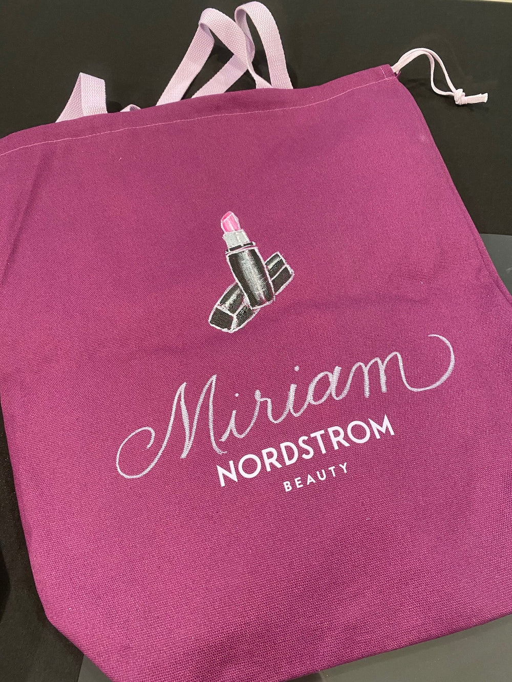 Hand-painted lipstick illustration and personalized name in elegant calligraphy on a Nordstrom Beauty canvas tote bag at a New York City event.