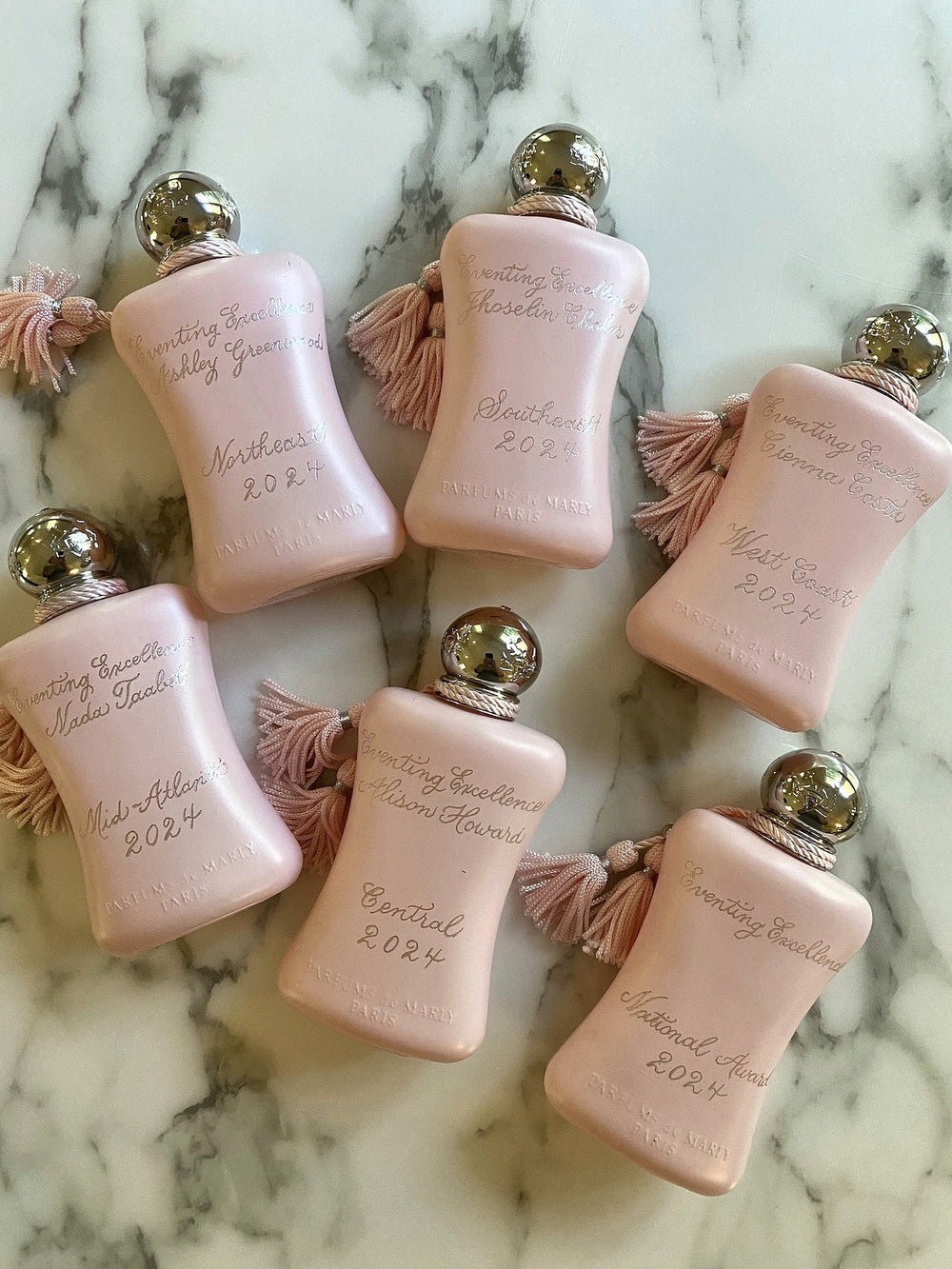 Collection of Parfums de Marly Delina perfume bottles hand engraved with personalized corporate award details in elegant calligraphy.