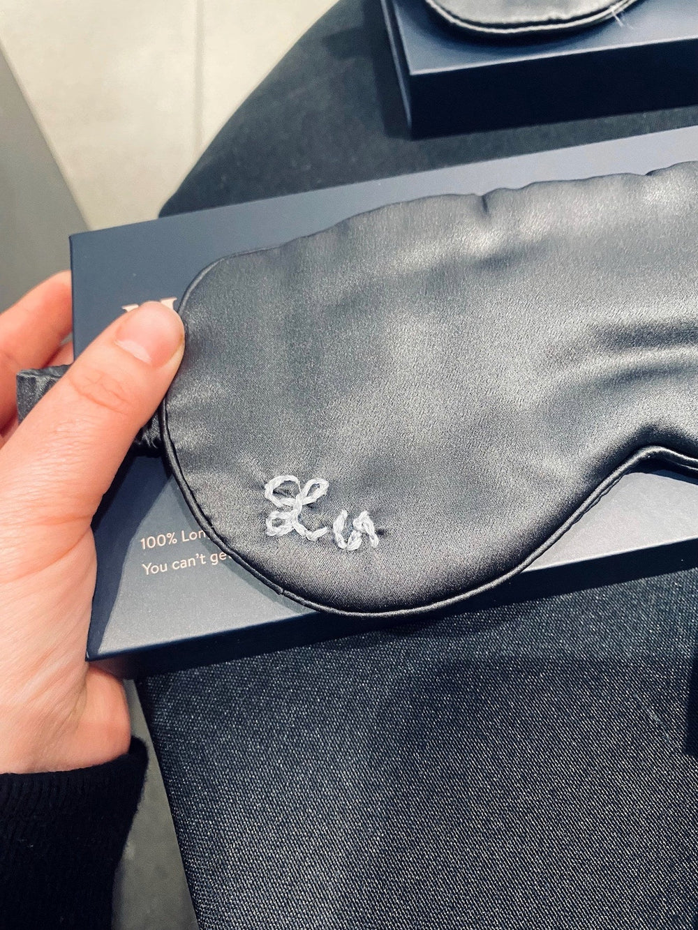 Hand-embroidered monogram in light blue thread on a black silk sleep mask during an Alo brand event.