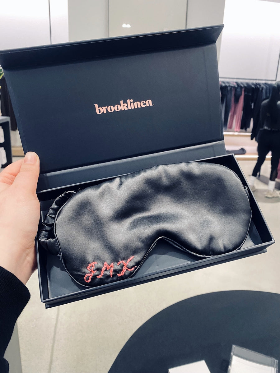 Black silk sleep mask with coral hand-embroidered initials presented in a Brooklinen gift box for an Alo brand event.
