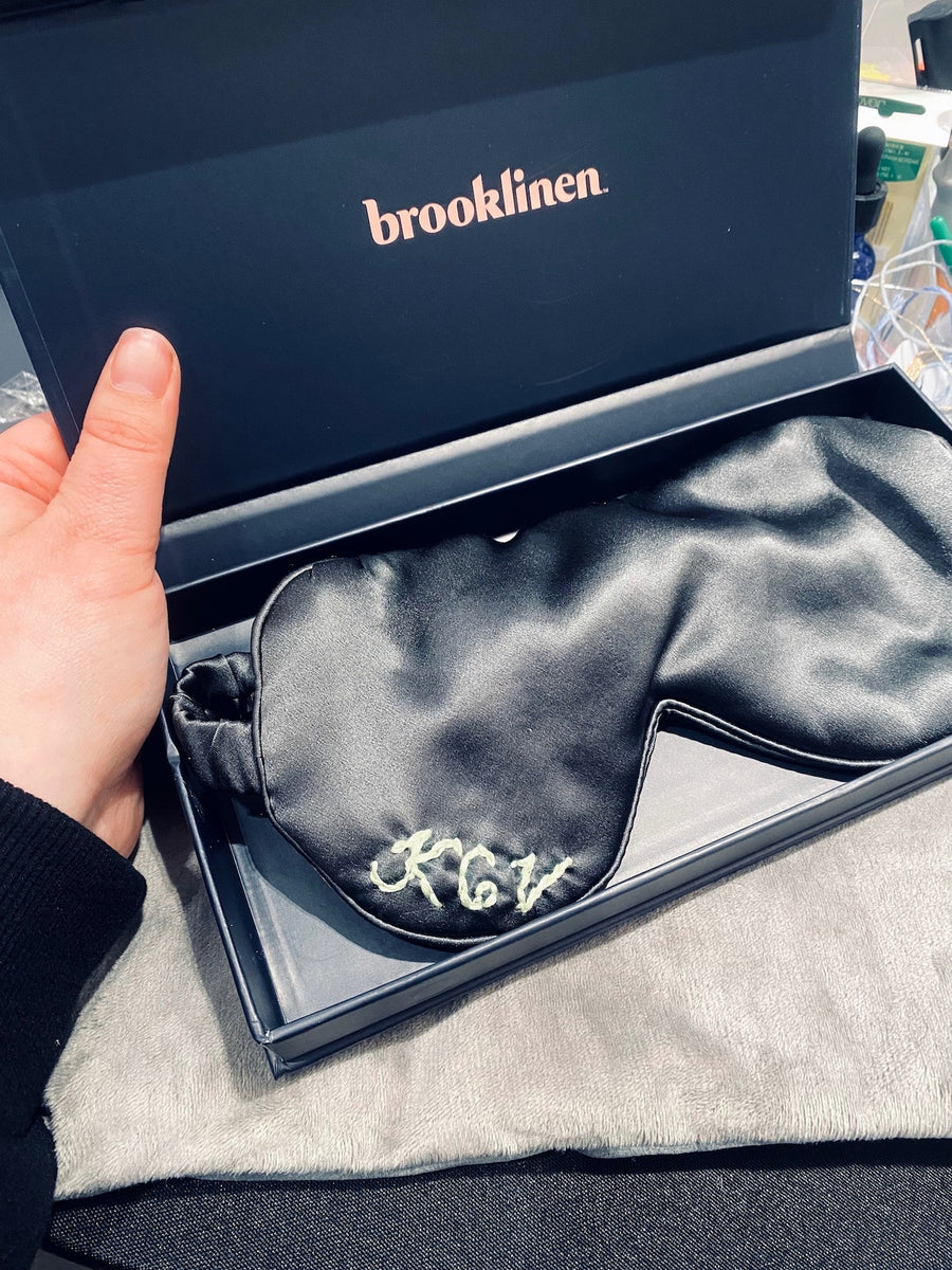 Custom embroidered initials on a black Brooklinen silk sleep mask displayed in branded gift packaging.