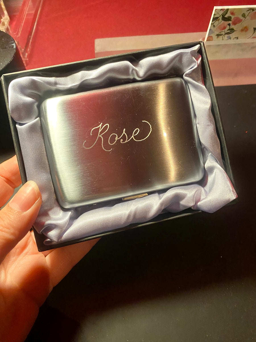 Custom hand engraved silver cigarette case with the name Rose, presented in a satin-lined gift box at a NYC event.