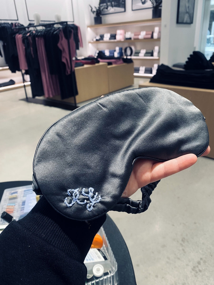 Hand-embroidered monogram in light blue thread on a black silk sleep mask during an Alo brand event.