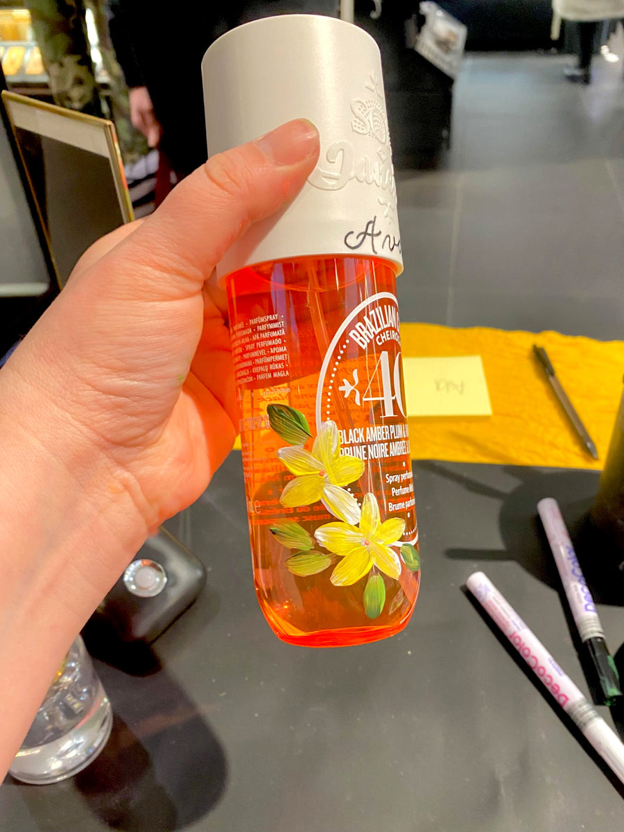 Sol de Janeiro Brazilian Crush Cheirosa 40 body mist decorated with hand-painted yellow plumeria flowers at a live retail event.