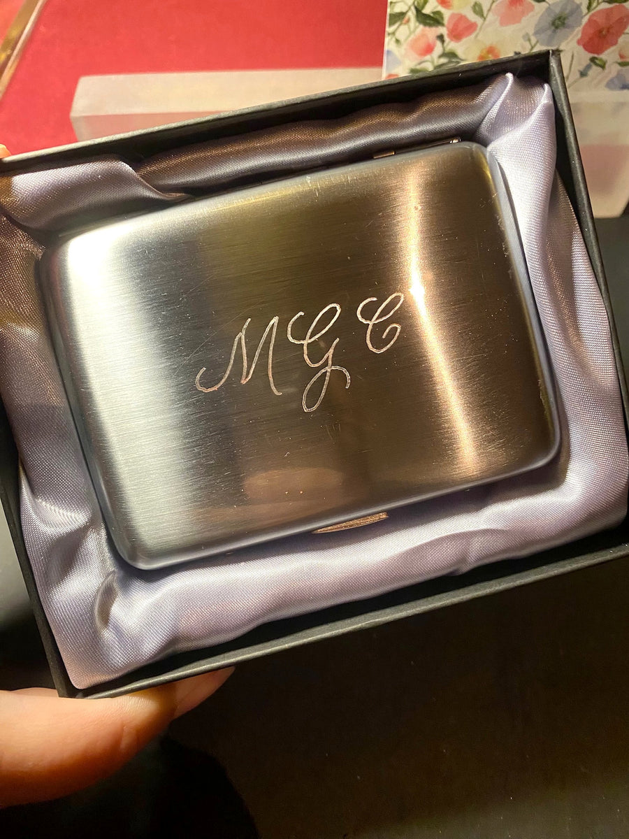 Close-up of a silver cigarette case personalized with an engraved script monogram for a luxury NYC event.