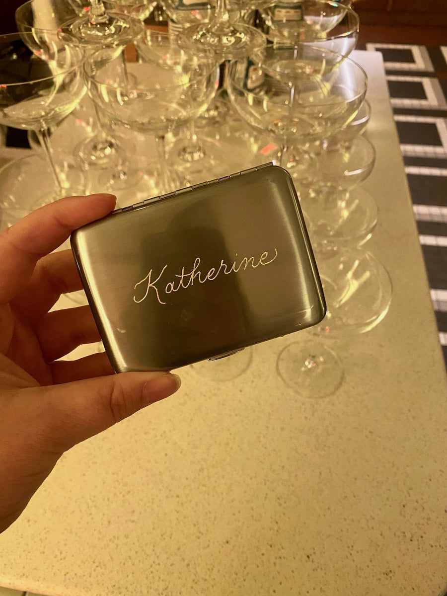Custom silver cigarette case hand engraved with the name Katherine in elegant script for So & So's Piano Bar opening.