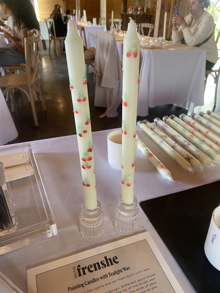 Hand-painted taper candles featuring colorful cherry designs at a Being Frenshe experiential brand event.