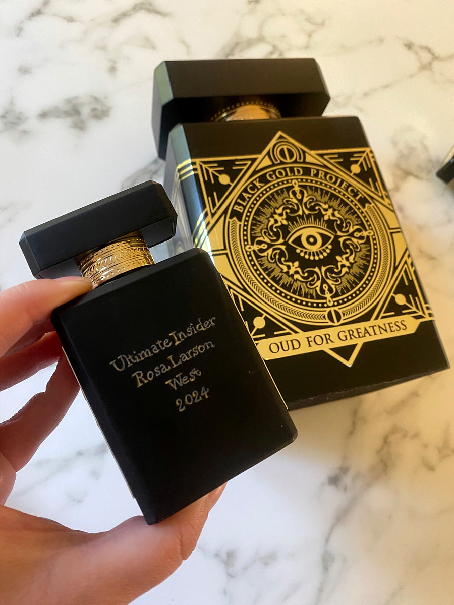 Black Initio Parfums Privés fragrance bottle with personalized gold engraving beside Black Gold Project packaging.